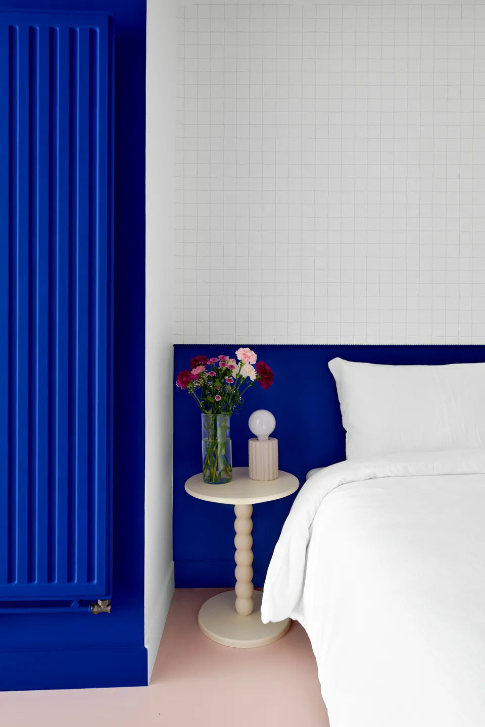 Studio Madame : architecte d’intérieur, Paris et Montmorency.
Projet réalisé à Deuil-la-Barre.
Photographie d’intérieur : arche et soubassement (tête de lit) peints en bleu Klein (Ressource) intégrant un espace nuit agrémenté d’un papier peint minimaliste quadrillé (Season Paper), d’une lampe et table de chevet beiges aux lignes originales et d’un lit avec parure blanche. Les murs sont peints en blanc et bleu Klein (Ressource) et le sol est habillé d’un béton ciré rose (Harmony Béton).