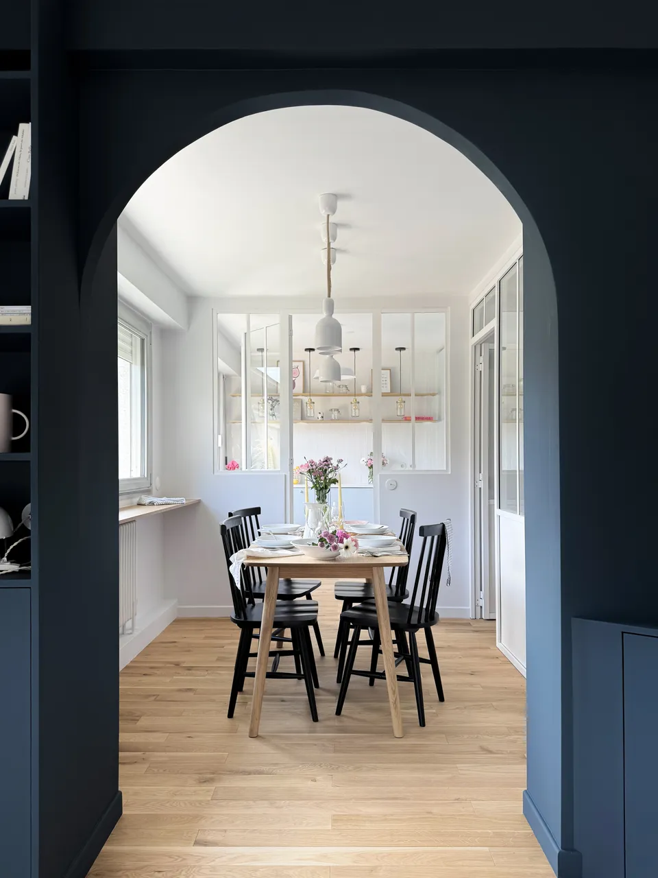 Studio Madame : architecte d’intérieur, Paris et Montmorency
Projet réalisé à Montmorency.
Photographie d’intérieur : salle à manger avec vue sur cuisine, composée d’une table rectangulaire avec 4 chaises vintages noires. La table est dressée et des suspensions tombent au-dessus de la table. La cuisine de couleur bleu ciel est visible en transparence grâce à la verrière atelier séparant les deux espaces.
